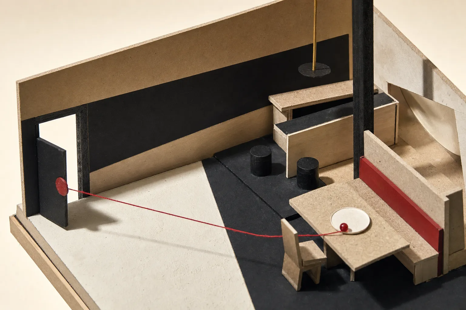 A chipboard model of a restaurant interior, one table set with a turned-wood plate and a glass bead, a red thread running from the door across the floor to it.